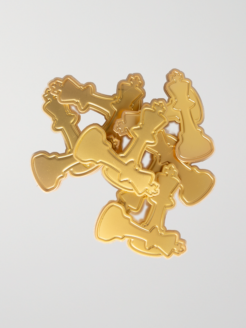  A cluster of goldtone Checkmate Anywear brooch pins is displayed on a white background. The pins are arranged aesthetically to showcase their etched gold details and refined finish. 