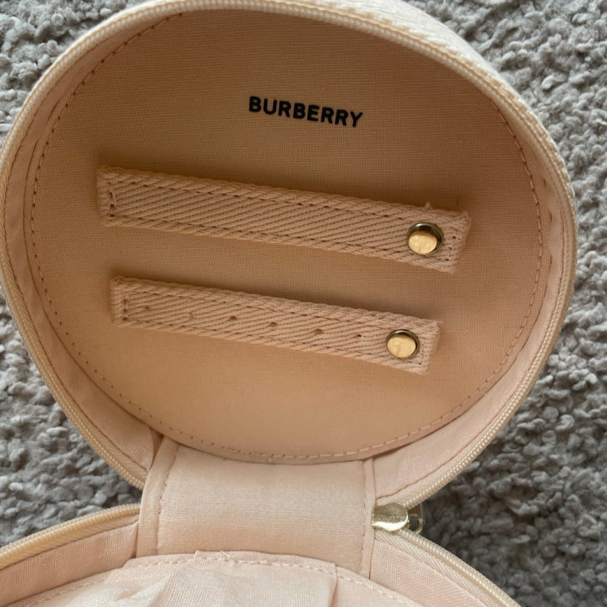 Open beige jewelry box with 'Burberry' branding on a textured surface.