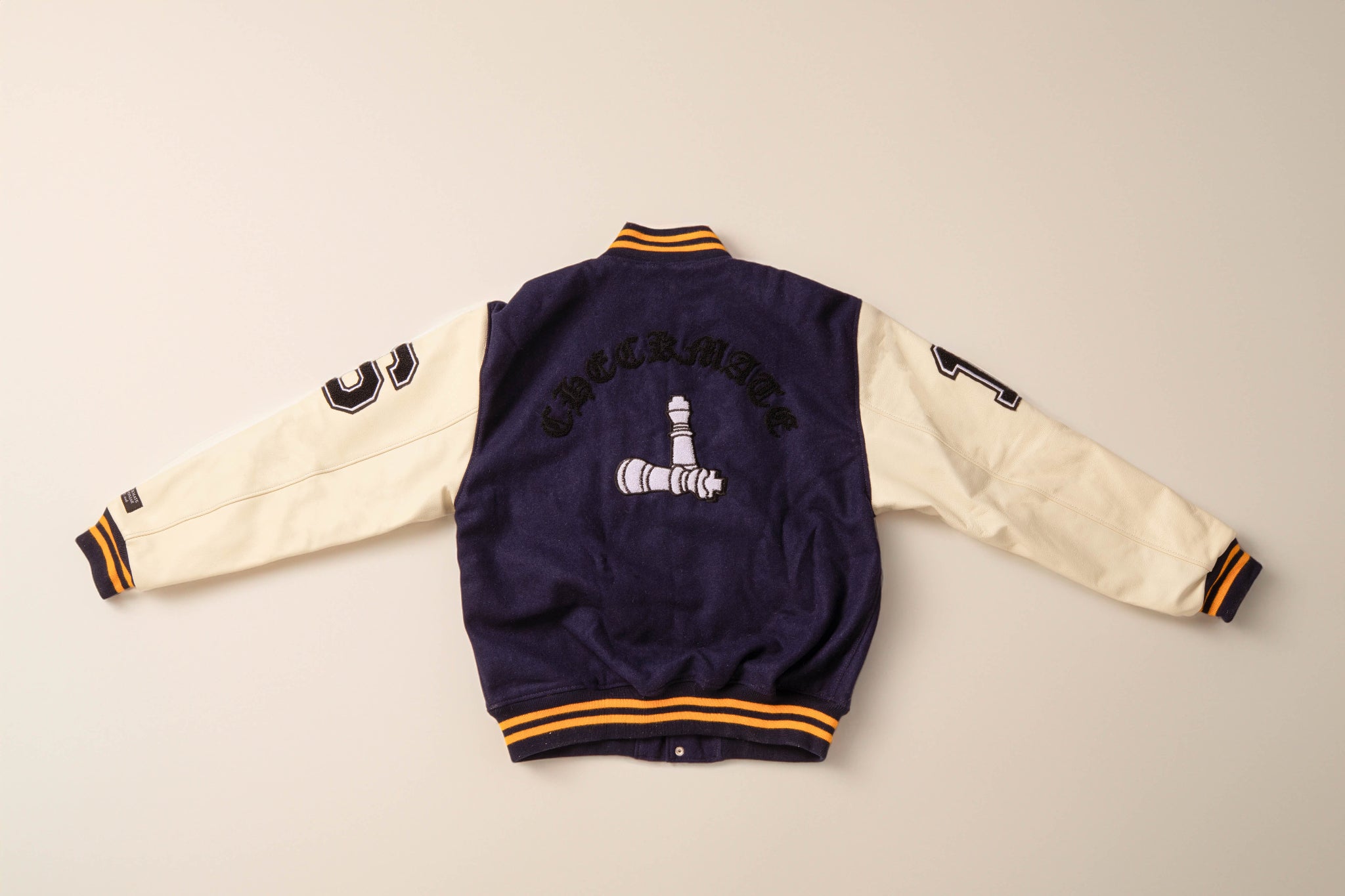 Checkmate anywear navy and yellow varsity jacket with embroidered design on neutral background