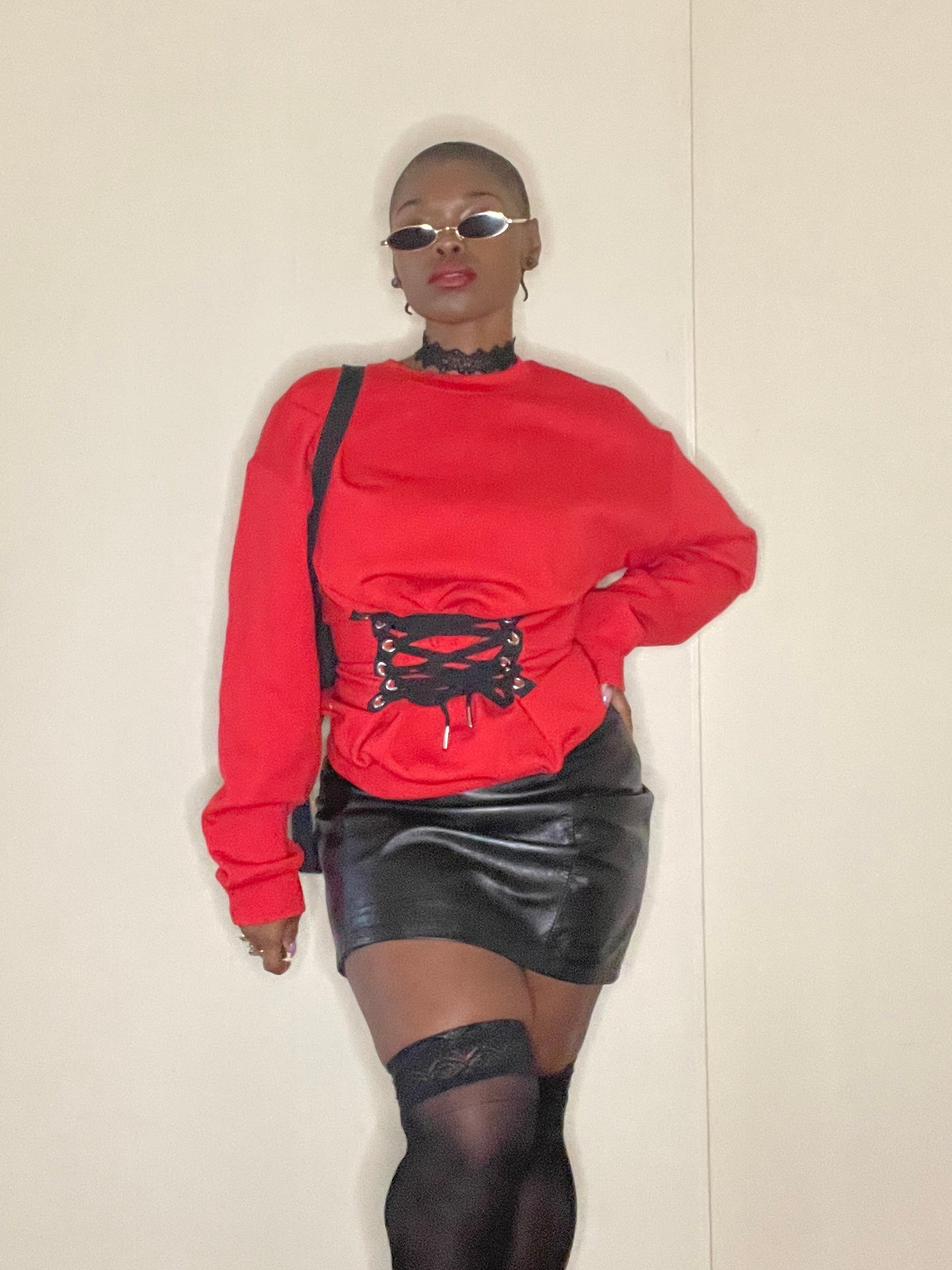 Person wearing a red sweater with black lace details and a black leather skirt against a plain background