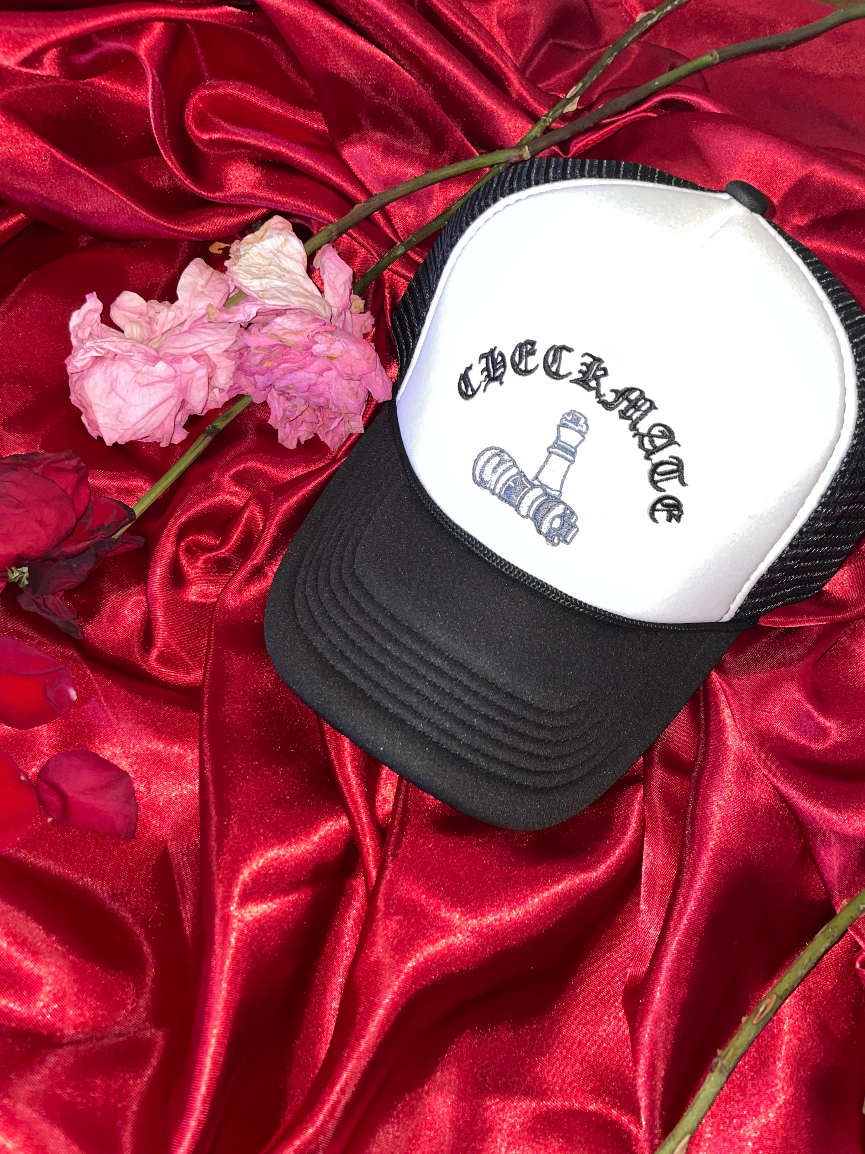 checkmate anywear black and white cap with text and graphics on a red satin surface with pink flowers and branches.