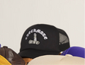 Black checkmate anywear trucker hat with white text on a gray background