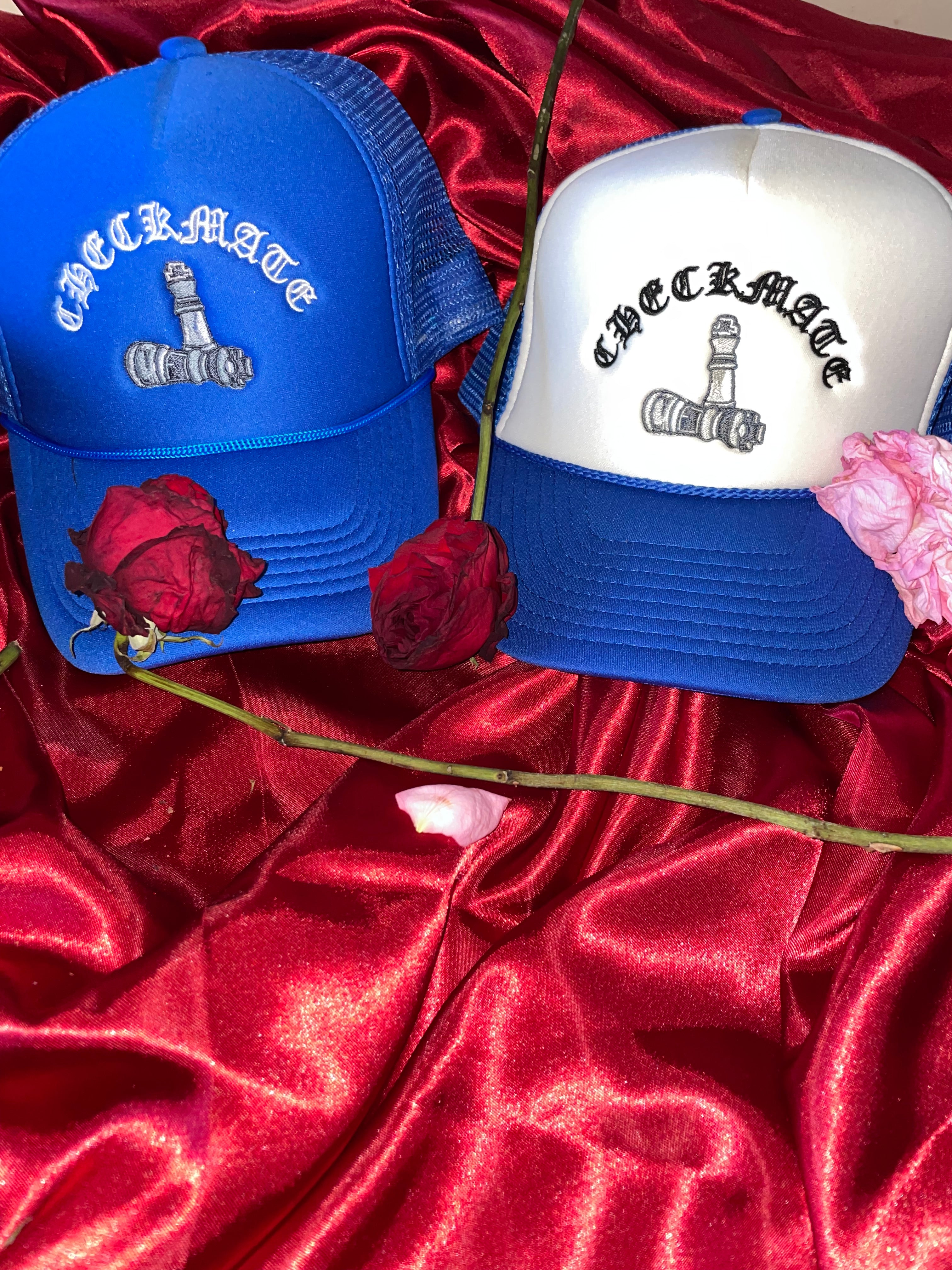 Two checkmate anywear trucker hats with text and graphics on a red satin background with flowers.