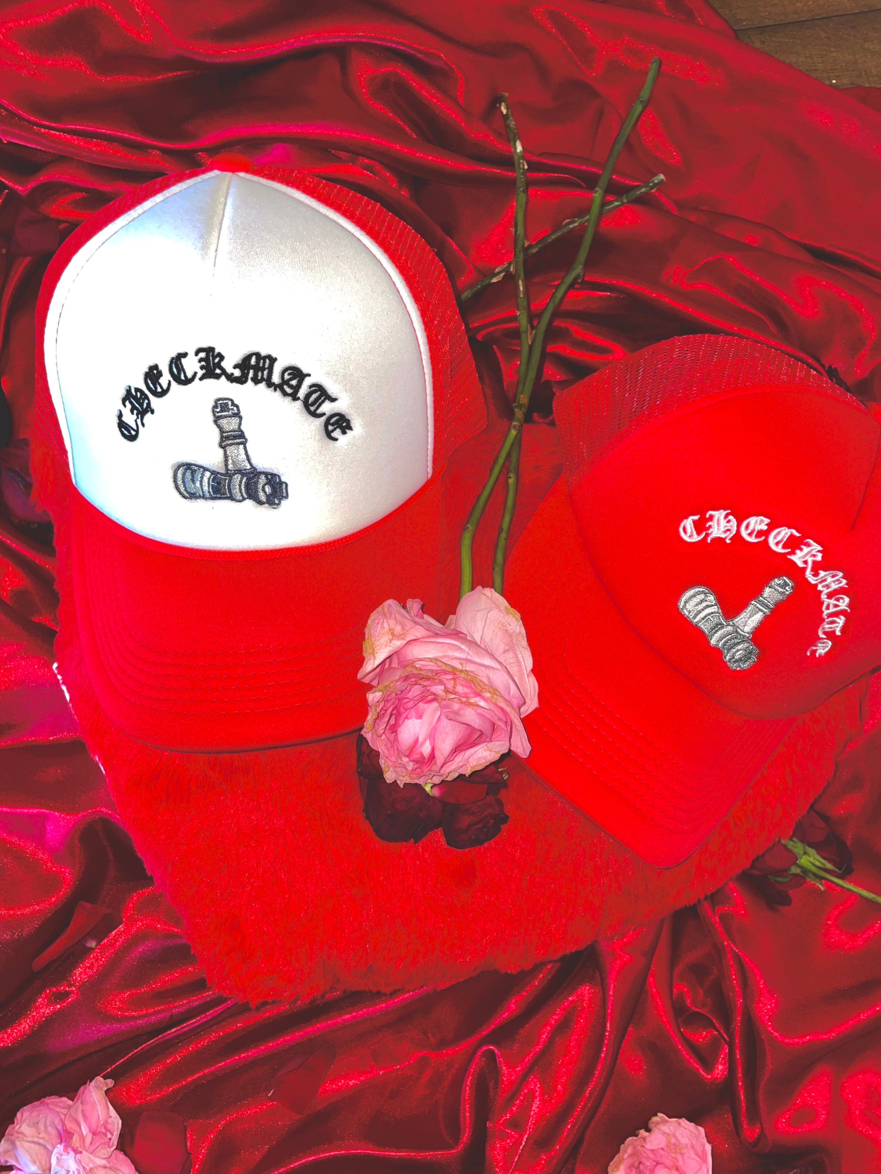 Two red checkmate anywear trucker hats featuring checkmate chess piece logo on a red satin background with pink roses.