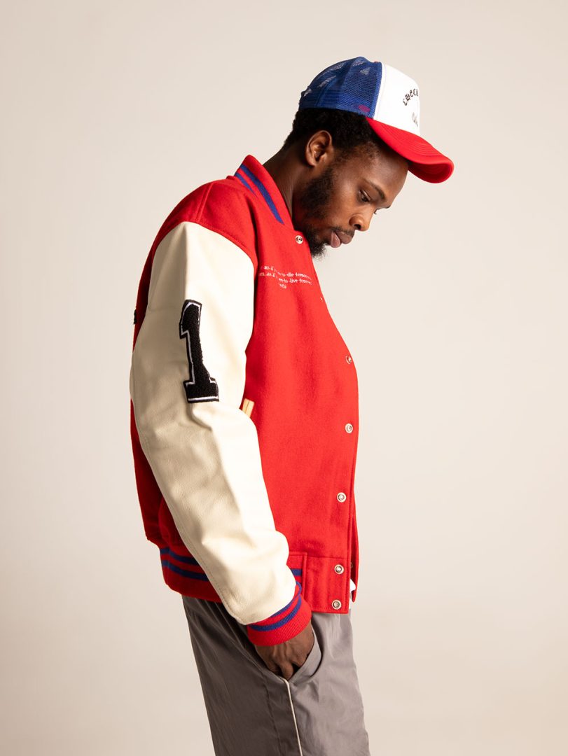 Person wearing a red and beige varsity jacket with a number on a plain background