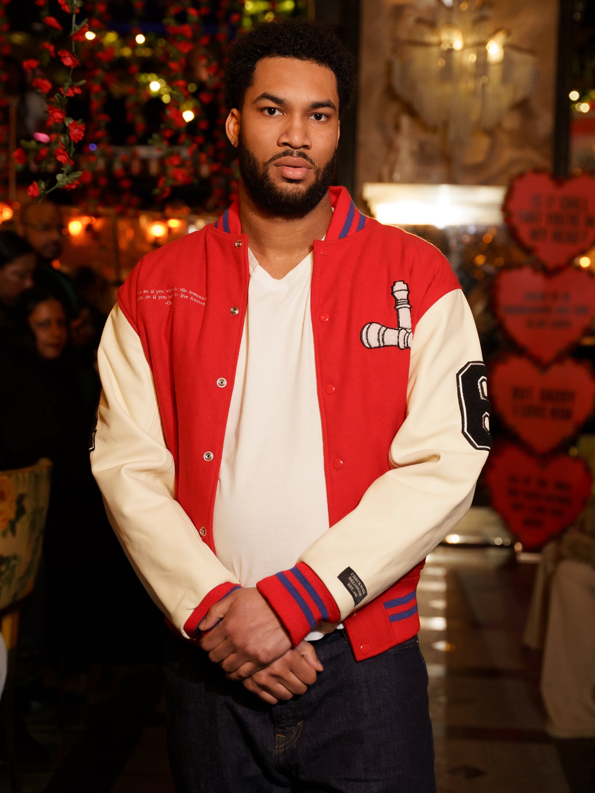Man wearing a red and blue varsity jacket with a white shirt underneath.