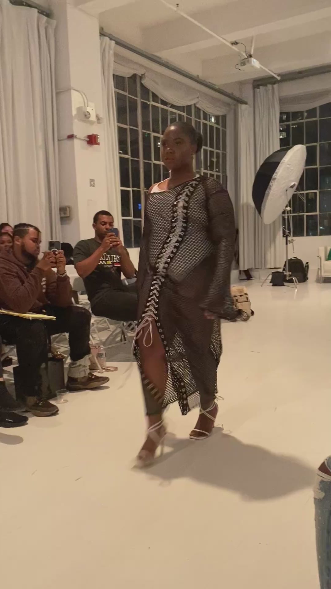 Model in black mesh long sleeve dress with laced front  detail walking runway